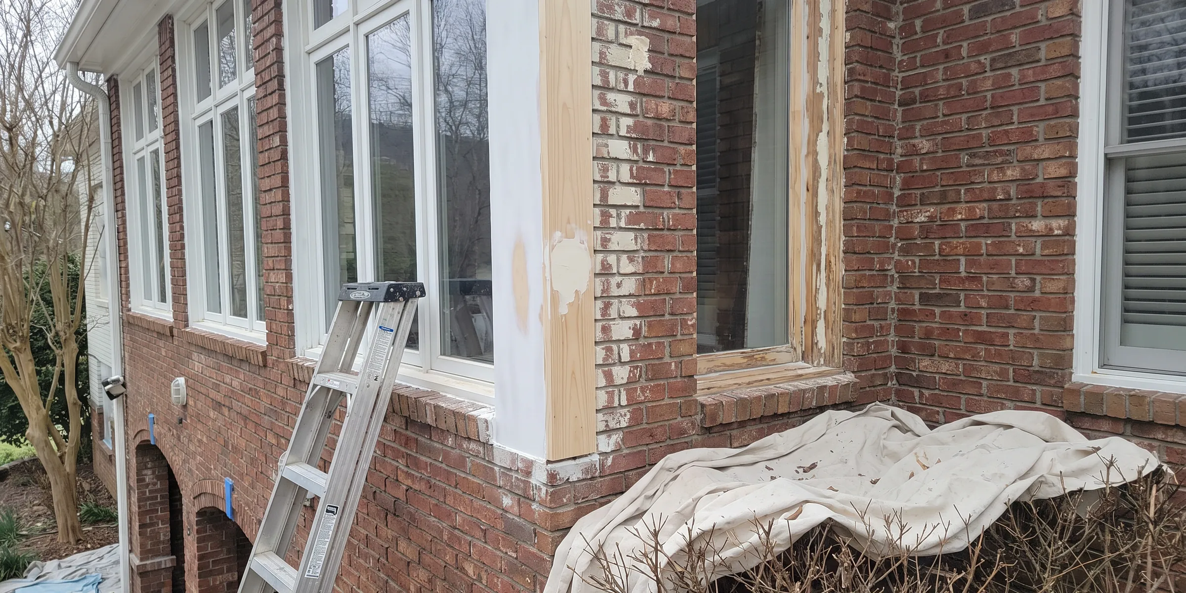 Carpentry repair on a window surround: fresh primed wood fitted where the old paint was scraped back