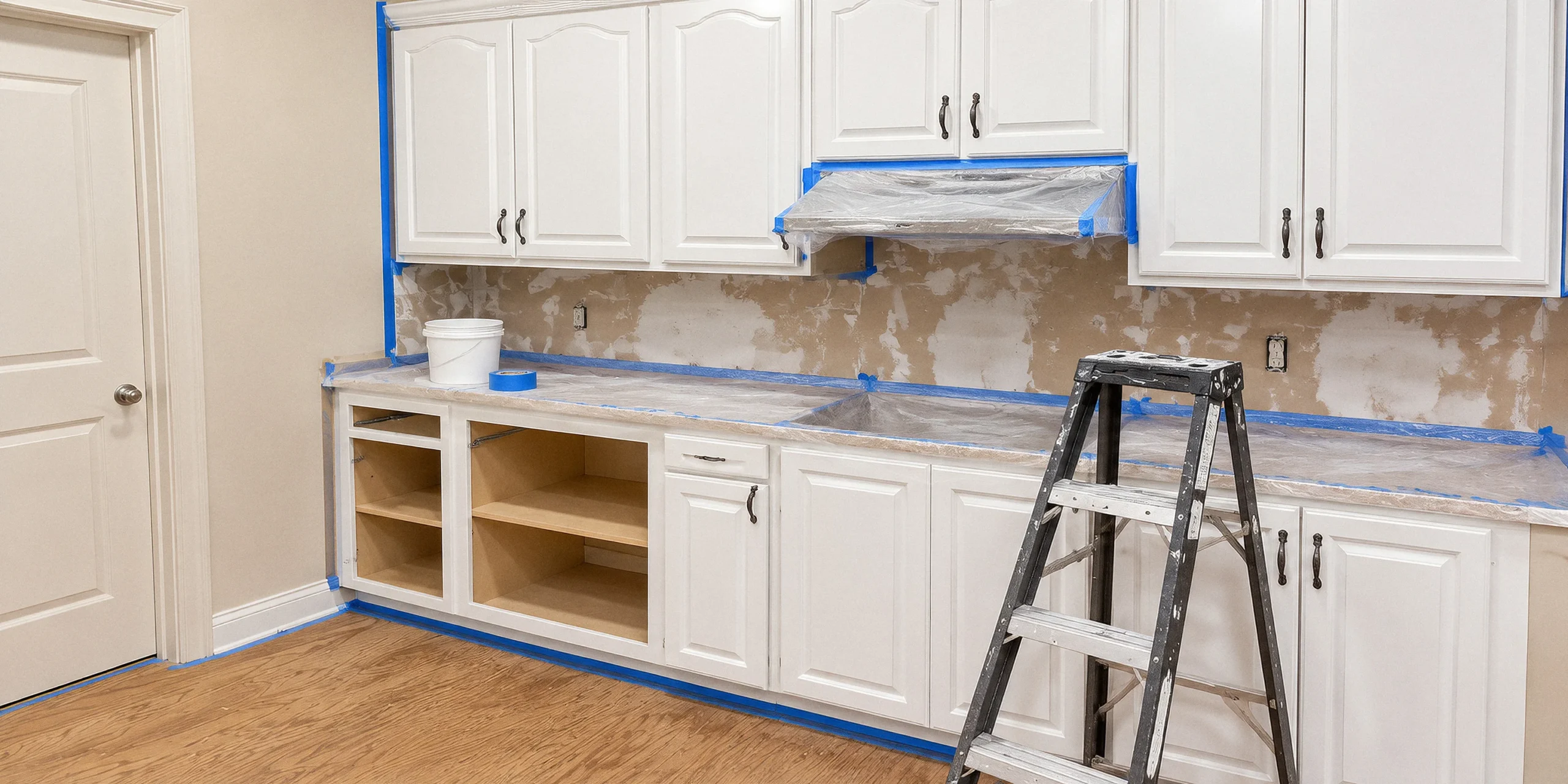 Cabinet doors and boxes partway through refinishing, taped and masked with a step ladder in the room