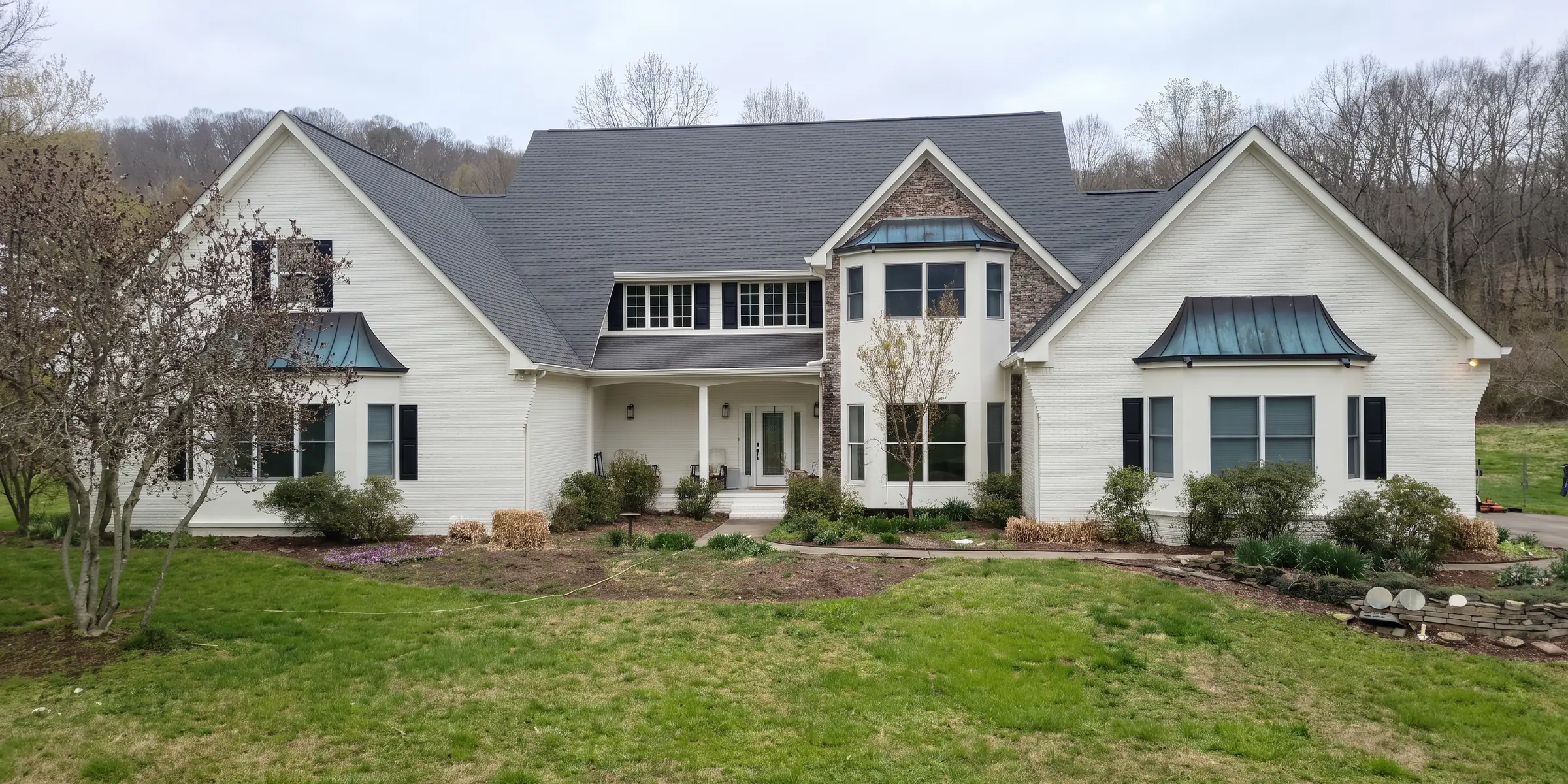 The front elevation of a house finished in a soft warm white, photographed from the lawn on an overcast spring day