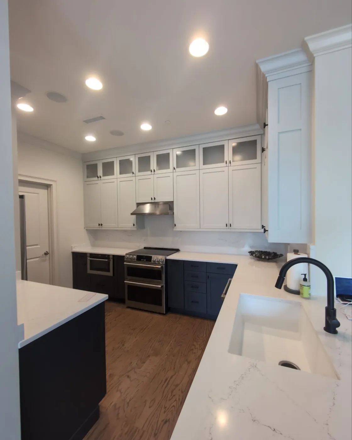 A refinished kitchen with white upper cabinets, navy lower cabinets and a marble island