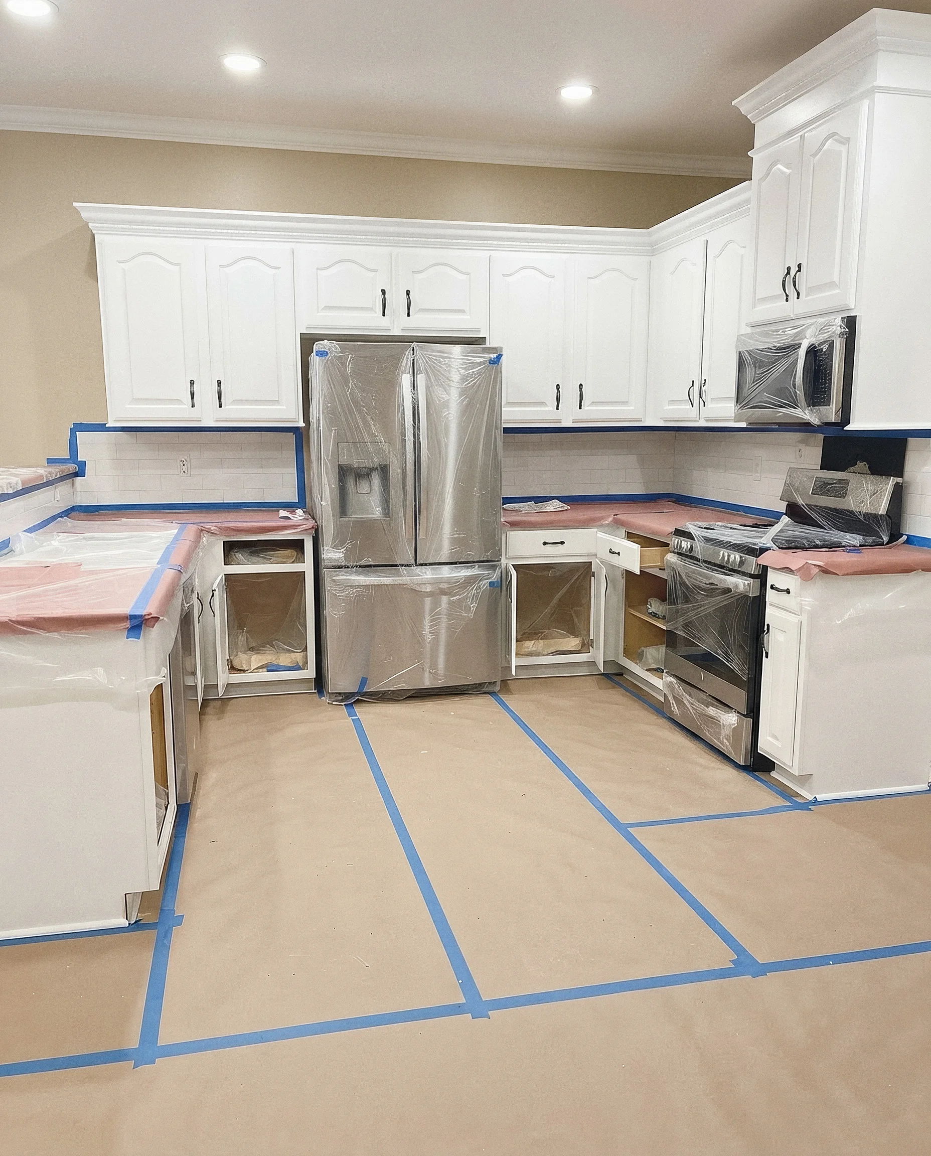 A kitchen protected for painting, with counters and floors papered and taped and the appliances wrapped