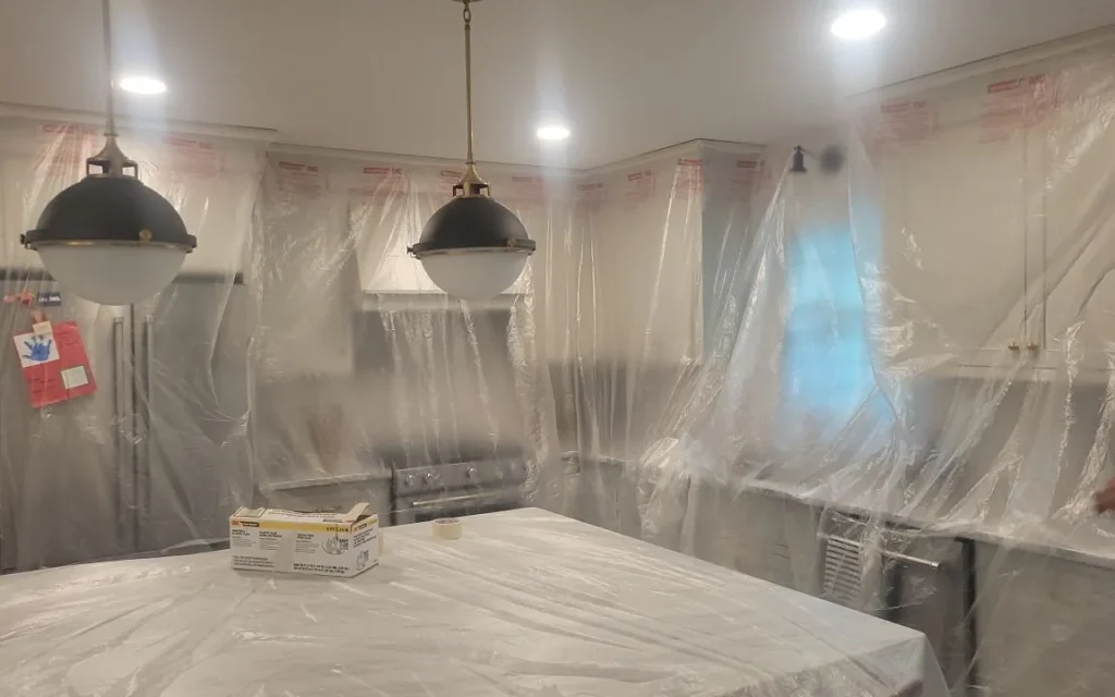 A kitchen wrapped in protective sheeting, pendant lights covered, before painting